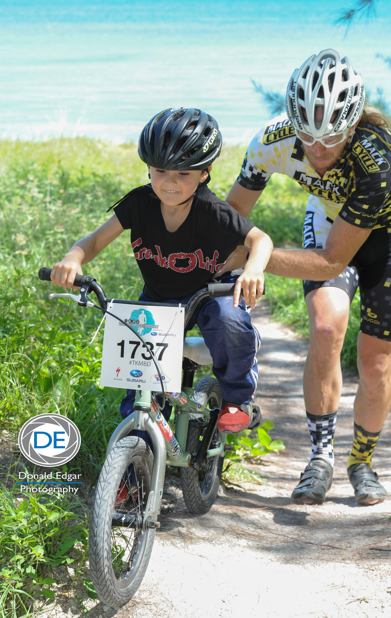 Kid learns to ride up big sandy hill at the beach front Virginia Key Mountain Bike Trails in Miami. He is helped up by Nixon Nixon, a Cannondale Cyclist.