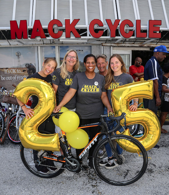 Georgia Johnson Celebrating her 25th Anniversary working at Mack Cycle in Miami. She is posing with the Mack Cycle Family who just gifted her a new Giant Road Bicycle. They are are pictured together with the bike and gold balloons that read "25"