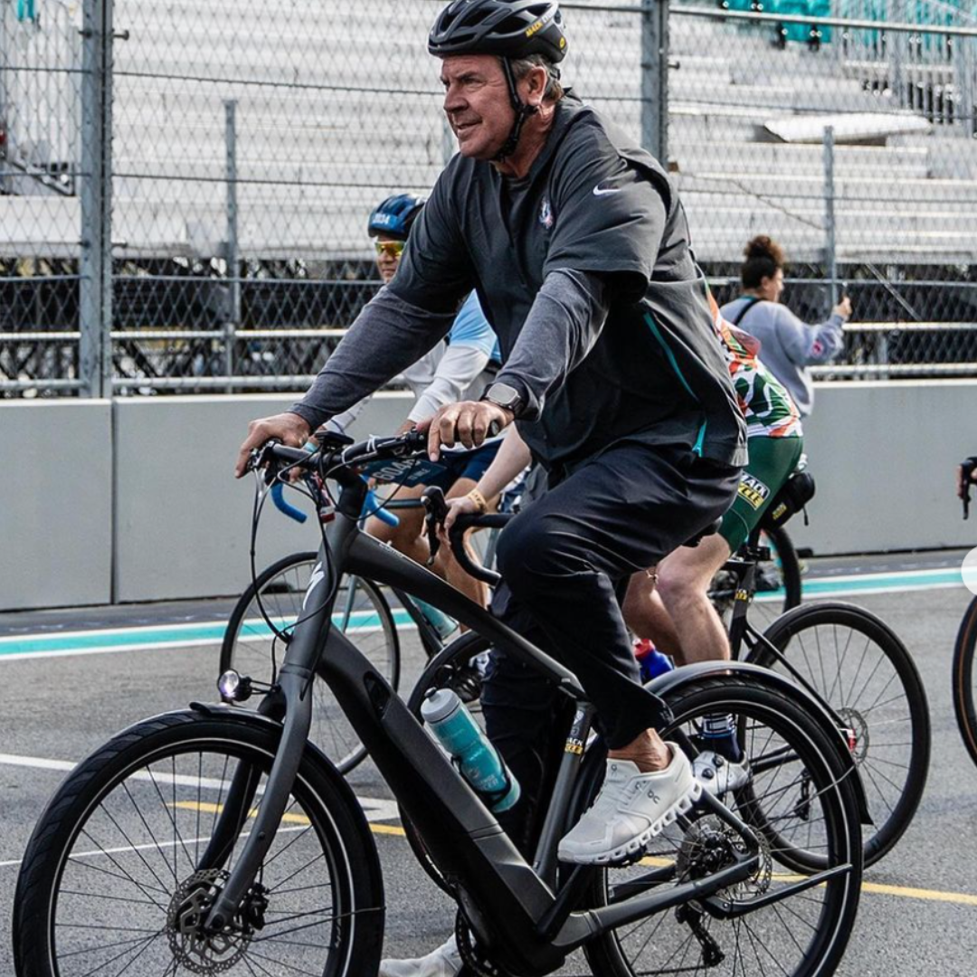 Dan Marino riding a Turbo Como from Mack Cycle during the Dolphins Challenge Cancer 2024, with the Formula 1 race track in the background.