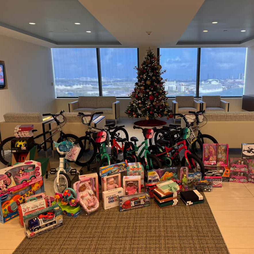 Room with toys and bicycles in front of a Christmas tree with a cityscape view at Foley & Lardner in Miami.