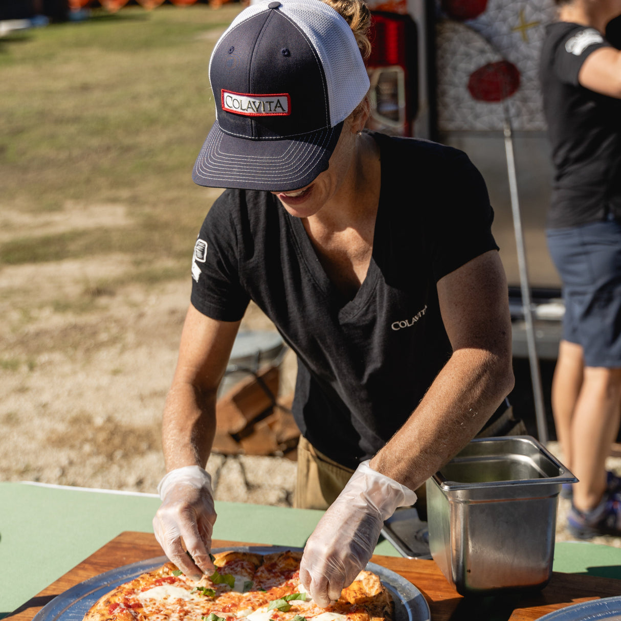 Mary Zider preparing a pizza outdoors from the colavita brick oven pizza truck with a casual setting at the mack cycle gravel event in miami